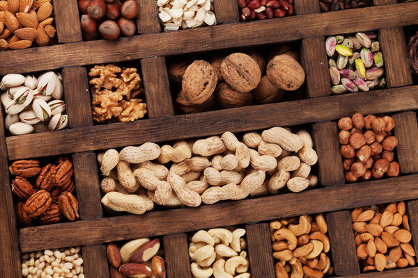 Разнообразный выбор орехов: арахис, фундук, каштан, грецкие орехи, фисташки и пеканы в деревянной коробке. Вид сверху
