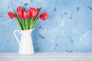 Mavi taş duvar önünde sürahi içinde kırmızı lale buketi. Kopya alanı ile