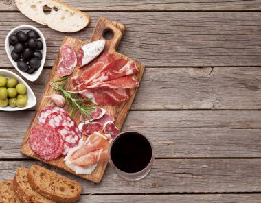Salam, dilimlenmiş jambon, sosis, jambon, pastırma, tost, zeytin. Et meze tabağı ve ahşap masa üzerinde kırmızı şarap. Kopya alanı ile Üstten Görünüm