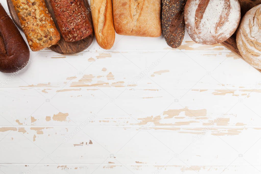 Various crusty bread and buns on white wooden background. Top view with space for your text