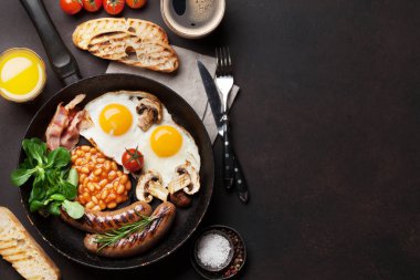 İngiliz kahvaltısı. Kızarmış yumurta, sosis, pastırma, fasulye, tost, domates, portakal suyu ve kahve fincanı taştan masada. Kopya alanı ile Üstten Görünüm