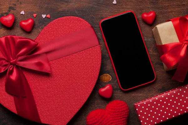 Valentine's day greeting card with heart gift boxes and smartphone on wooden background. Top view with space for your greetings or smart phone app. Flat lay