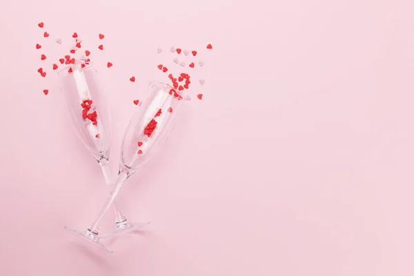 Champagne glasses and heart shaped sweets holiday template. Christmas, Birthday or Valentines'day over pink background. Top view with space for your greetings. Flat lay