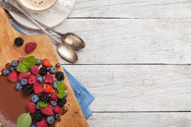 Böğürtlenli çikolatalı kek ve kahve fincanı. Kopya alanı olan ahşap masada. Üst görünüm düzlüğü