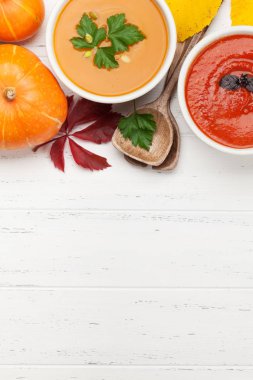 Tomato and pumpkin vegetable soup and autumn leaves on wooden backdrop. Top view with copy space. Flat lay