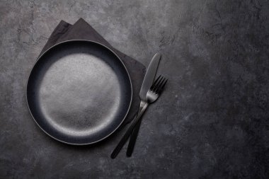Boş tabak, çatal ve bıçak. Siyah mutfak gereçleri taş masaya dizilmiş. Üst görünüm düzlüğü kopyalama alanı ile yatıyordu