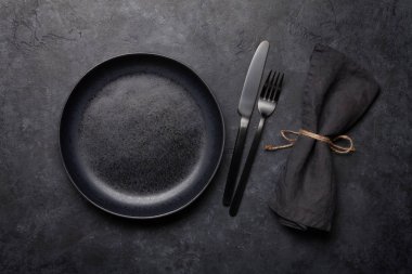 Boş tabak, çatal ve bıçak. Siyah mutfak gereçleri taş masaya dizilmiş. Üst görünüm düzlüğü kopyalama alanı ile yatıyordu