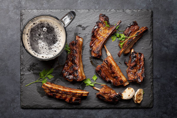 Barbecue beef ribs with bbq sauce sliced on a stone board with beer mug. Top view flat lay