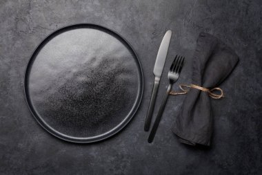 Boş tabak, çatal ve bıçak. Siyah mutfak gereçleri taş masaya dizilmiş. Üst görünüm düzlüğü kopyalama alanı ile yatıyordu