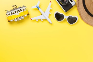 Güneş şapkası, güneş gözlüğü, tramvay ve uçak oyuncağı ile sarı güneşli zemin üzerinde seyahat konsepti. Üst görünüm düzlüğü kopyalama alanı ile yatıyordu
