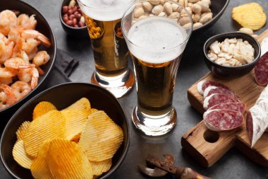 Taslak bira ve taş arka plan üzerinde aperatifler. Fındık, cips, sosis ve karides