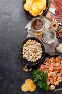 Taslak bira ve taş arka plan üzerinde aperatifler. Fındık, cips, sosis ve karides. Düz yatıyordu. Kopyalama alanı ile üstte görünüm