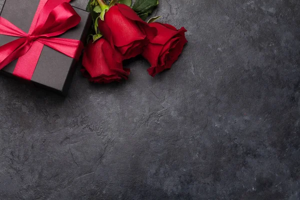 Valentines day greeting card with rose flowers bouquet and gift box over stone background with space for your greetings. Top view flat lay