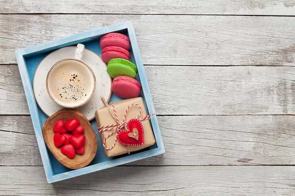 Valentines day greeting box with coffee cup, macaroons and gingerbread cookies over wooden background with space for your greetings. Top view flat lay