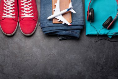 Uçak oyuncakları, giysiler ve seyahat aksesuarları. Spor ayakkabı, kot pantolon, kulaklık ve uçak. Turist ve tatil şeyleri taştan arka planda, mesajın için yer var. Üst görünüm düzlüğü