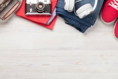 Bavul, kamera, kıyafetler ve seyahat aksesuarları. Spor ayakkabı, kot pantolon, kulaklık ve kamera. Turist ve tatil şeyleri ahşap arka planda, mesajın için yer var. Üst görünüm düzlüğü