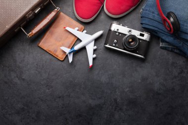 Bavul, kamera, kıyafetler ve seyahat aksesuarları. Spor ayakkabı, kot pantolon, kulaklık ve kamera. Turist ve tatil şeyleri taştan arka planda, mesajın için yer var. Üst görünüm düzlüğü