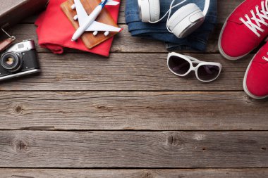 Bavul, kamera, kıyafetler ve seyahat aksesuarları. Spor ayakkabı, kot pantolon, kulaklık ve güneş gözlüğü. Turist ve tatil şeyleri ahşap arka planda, mesajın için yer var. Üst görünüm düzlüğü
