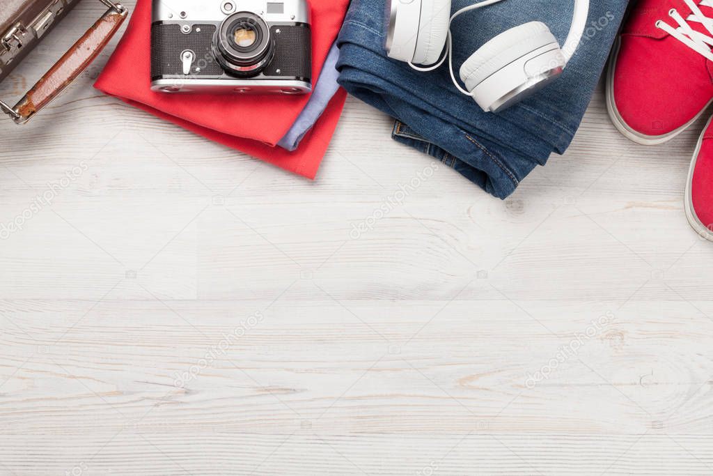 Suitcase, camera, clothes and travel accessories. Sneakers, jeans, headphones and camera. Tourist and vacation things on wooden background with space for your text. Top view flat lay
