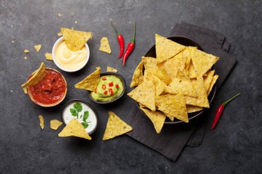 Çeşitli soslu Meksika cipsi. Guacamole, salsa, peynir ve ekşi krema. Üst görünüm düz taş masa üzerinde yatıyordu