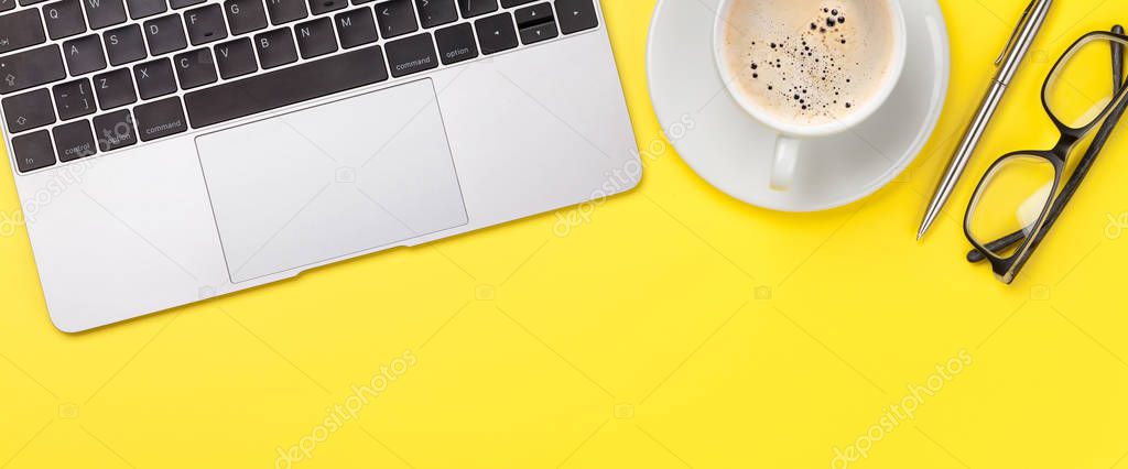 Office yellow workplace backdrop with coffee cup, supplies and computer. Wide flat lay. Top view with copy space for your goals