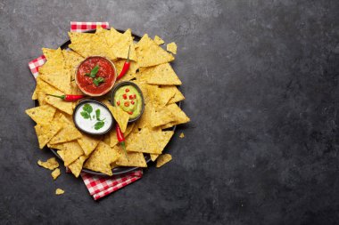 Çeşitli soslu Meksika cipsi - guacamole, salsa ve ekşi krema. Üst görünüm düz taş masa üzerinde kopya alanı ile yatıyordu