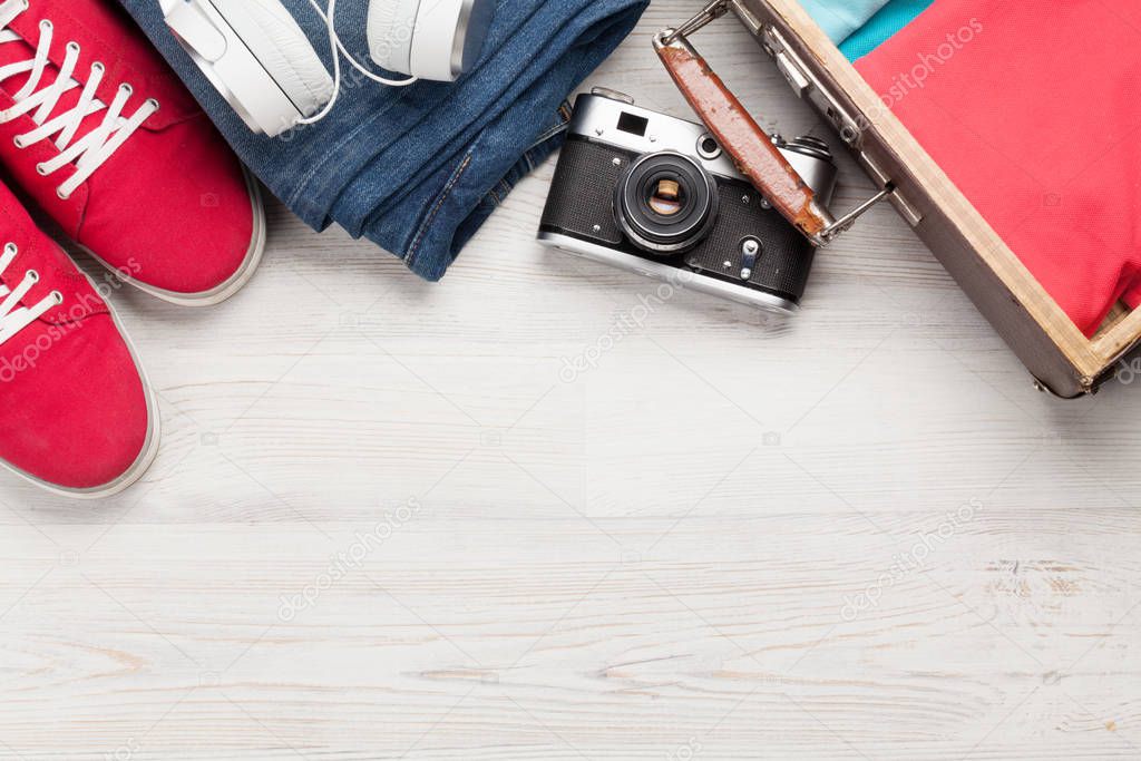 Suitcase, camera, clothes and travel accessories. Sneakers, jeans, headphones and camera. Tourist and vacation things on wooden background with space for your text. Top view flat lay