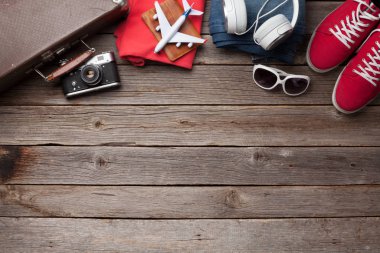 Bavul, kamera, kıyafetler ve seyahat aksesuarları. Spor ayakkabı, kot pantolon, kulaklık ve kamera. Turist ve tatil şeyleri ahşap arka planda, mesajın için yer var. Üst görünüm düzlüğü
