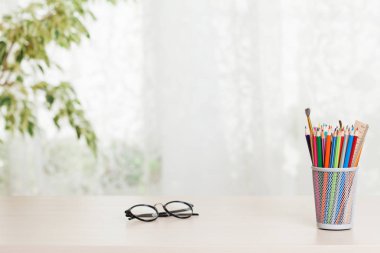 Home office workplace with glasses and supplies on table, houseplant and bright light from window
