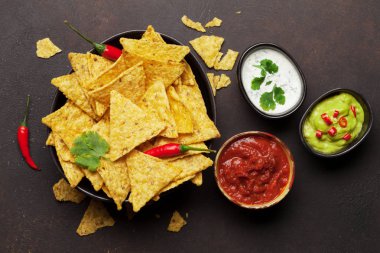 Mexican nachos chips with various sauces - guacamole, salsa and sour cream. Top view flat lay on stone table