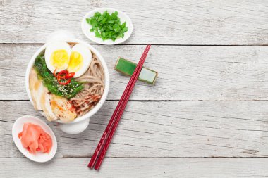 Asian noodle ramen soup with chicken, vegetables and eggs on wooden background. Top view flat lay with copy space