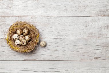 Easter greeting card with quail eggs in nest on wooden background. Top view flat lay with space for your greetings