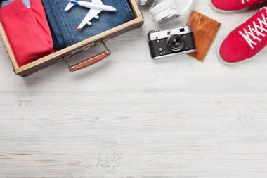 Bavul, kamera, kıyafetler ve seyahat aksesuarları. Spor ayakkabı, kot pantolon, kulaklık ve kamera. Turist ve tatil şeyleri ahşap arka planda, mesajın için yer var. Üst görünüm düzlüğü