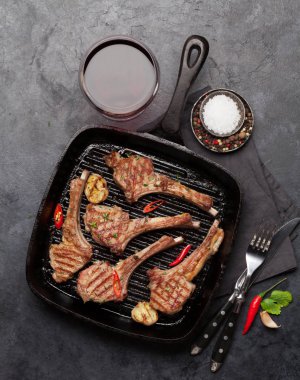 Kızartma tavasında ızgara kuzu pirzolası ve kırmızı şarap kadehi. Baharatlı ve baharatlı kuzu pirzolası. Taş masadaki üst görünüm