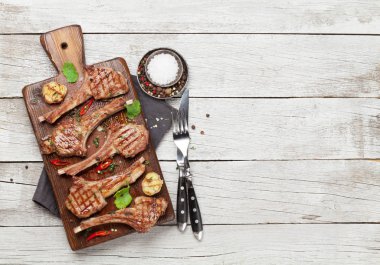 Grilled lamb ribs on cutting board. Hot rack of lamb with spices and condiments. Top view on wooden table with copy space