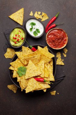 Mexican nachos chips with various sauces - guacamole, salsa and sour cream. Top view flat lay on stone table