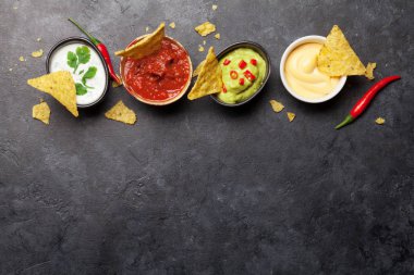 Çeşitli soslu Meksika cipsi. Guacamole, salsa, peynir ve ekşi krema. Üst görünüm düz taş masa üzerinde kopya alanı ile yatıyordu