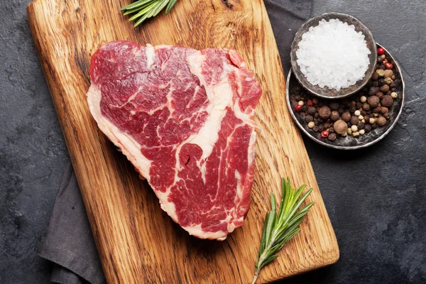 将新鲜的生牛肉牛排与调味品一起放在切菜板上 顶视图平铺 — 图库照片