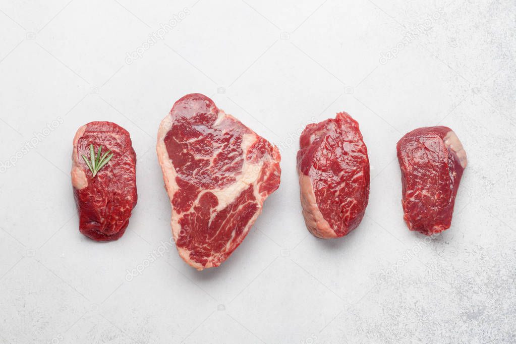 Variety of fresh raw beef steaks with spices on stone board. Top view flat lay with copy space