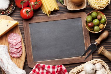 İtalyan mutfağı malzemeleri. Makarna, peynir, salam, zeytin ve yumurta. Üst görünüm düz tahta masa üzerinde yatıyordu kopyalama alanı için karatahta ile