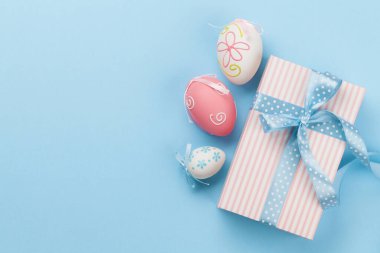 Hediye kutulu Paskalya tebrik kartı ve mavi arka planda renkli paskalya yumurtaları. Tebrik etmek için en üstteki dairede yer var.
