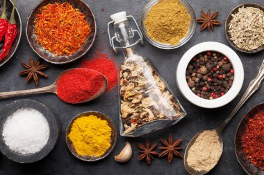 Koyu taş masada çeşitli baharatlar ve kaşıklar. Hint mutfağı. Üst görünüm düzlüğü