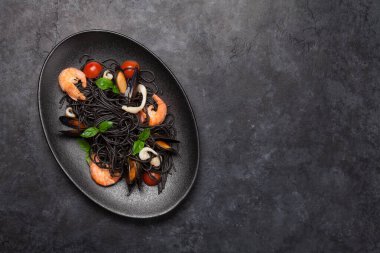 Deniz ürünleri, domates ve fesleğenli siyah spagetti makarna. Üst görünüm düzlüğü kopyalama alanı ile yatıyordu
