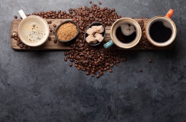 Kahve fincanları, şeker ve kavrulmuş fasulyeler koyu taş masada. Kopyalama alanı olan üst görünüm. Düz yatıyordu