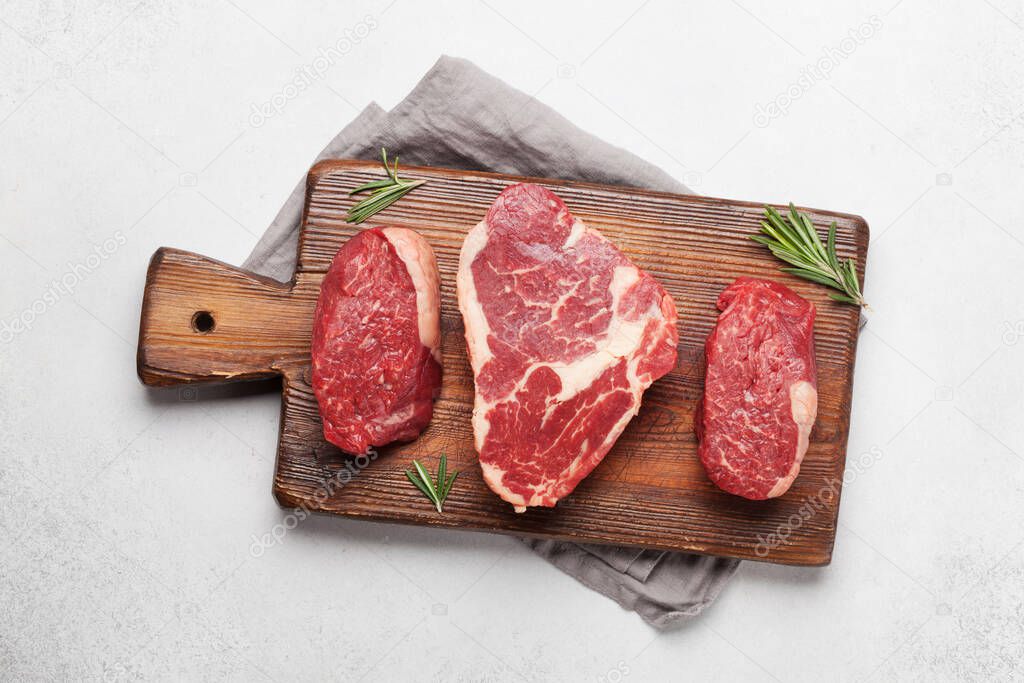 Variety of fresh raw beef steaks with spices on cutting board. Top view flat lay