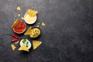 Çeşitli soslu Meksika cipsi. Guacamole, salsa, peynir ve ekşi krema. Üst görünüm düz taş masa üzerinde kopya alanı ile yatıyordu