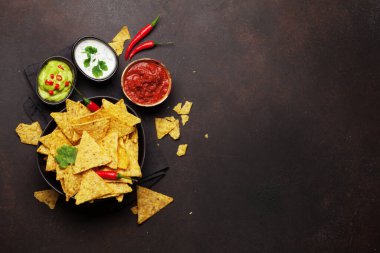 Çeşitli soslu Meksika cipsi - guacamole, salsa ve ekşi krema. Üst görünüm düz taş masa üzerinde kopya alanı ile yatıyordu