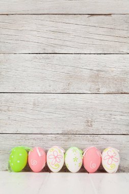 Ahşap duvarın önünde renkli paskalya yumurtaları olan Paskalya tebrik kartı. Selamlarınız için yer var.