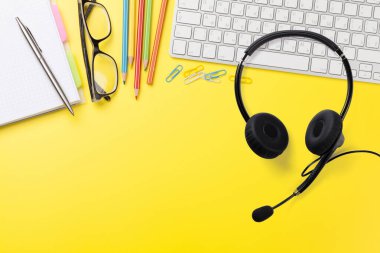 Ofis sarısı iş yeri, malzeme, kulaklık ve bilgisayar. Uzaktan arama ve buluşma konsepti. Hedefleriniz için fotokopi alanı olan üst görünüm düzlüğü