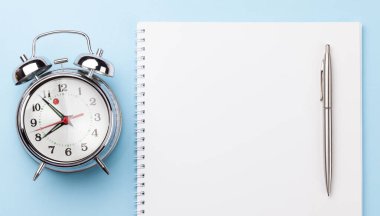 Malzemeleri ve çalar saati olan mavi çalışma masası. Sabah ya da teslim tarihi konsepti. Metnin için en üstte boşluk var. Düz yatıyordu